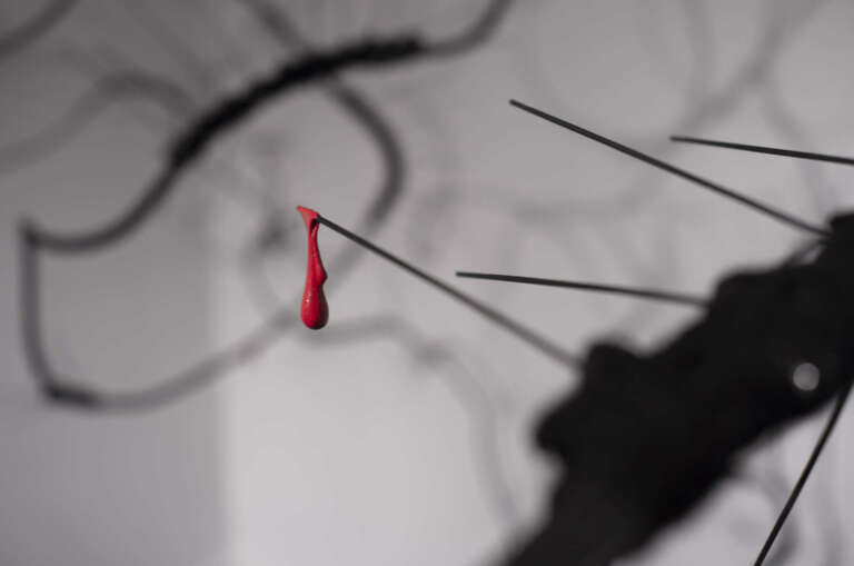 a close up of rotating spiked black wire sculpture with red drop